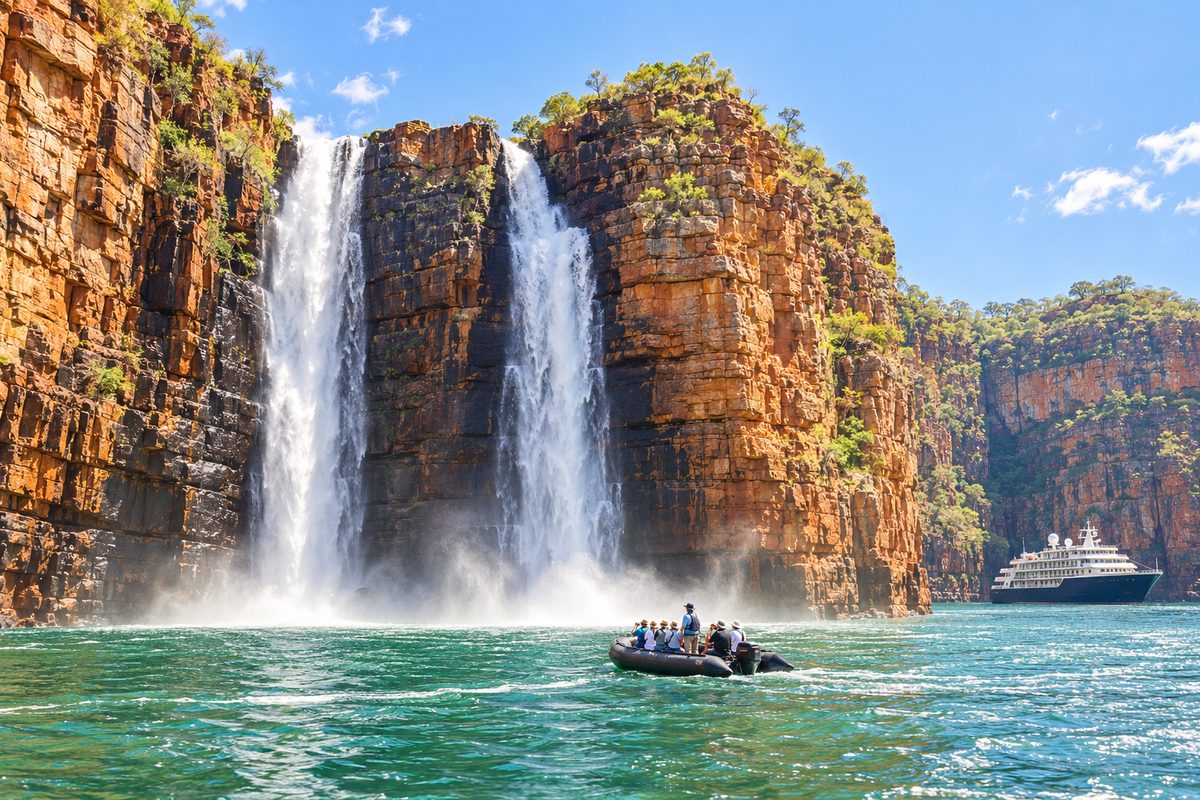 Twin waterfalls pouring down red cliffs in the Kimberley, a Zodiac below